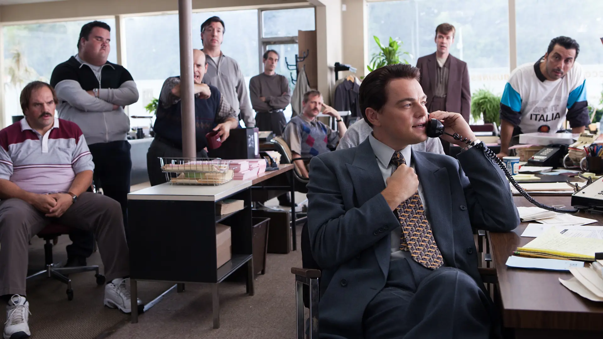 Cena do filme O Lobo de Wall Street: homem ao telefone em um escritório enquanto a equipe observa