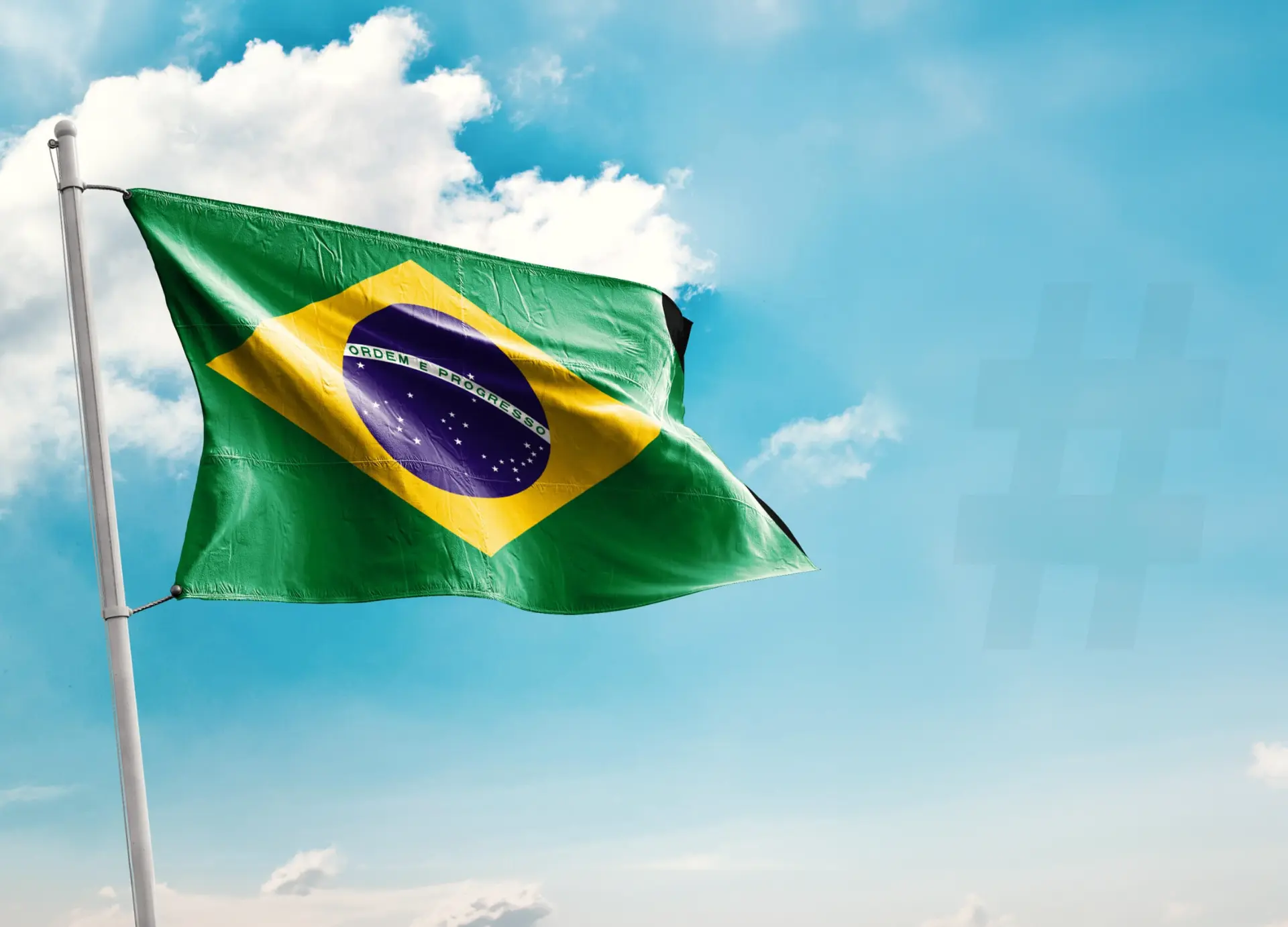 Bandeira do Brasil tremulando em um mastro contra um céu azul com nuvens